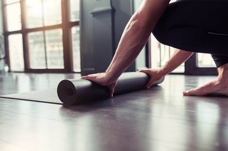 Mann will Beckenbodentraining machen und rollt dafür seine Gymnastikmatte aus. 